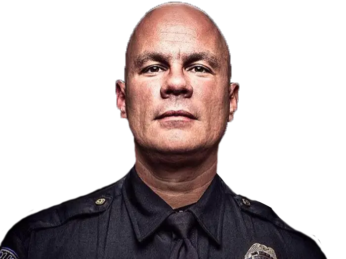 A serious-looking man wearing a dark police uniform and tie stands against a black background, facing the camera directly.